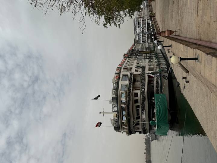A long Nile cruise ship moored at a riverside quay under a hazy sky.