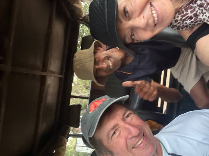 Three adults smiling inside a safari jeep, one giving a thumbs-up to the camera.