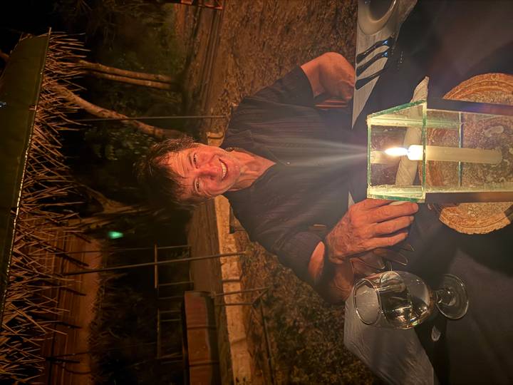 Man seated at an outdoor candlelit dinner table at night, smiling warmly.