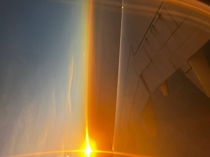 View from airplane wing of vibrant orange sunrise above cloud layers