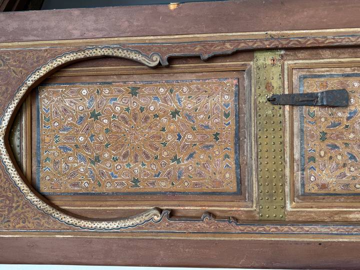 Close-up of a richly carved and painted wooden door with brass studs and latch