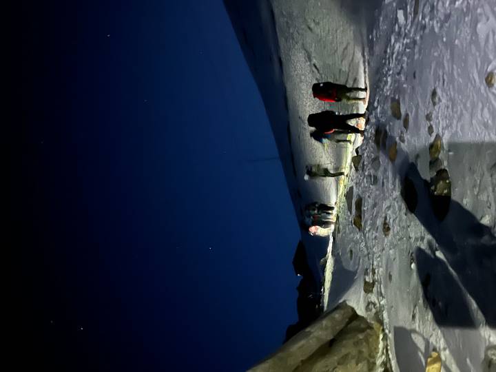 Early morning ascent with trekkers using headlamps on a snowy mountain trail under a dark starry sky