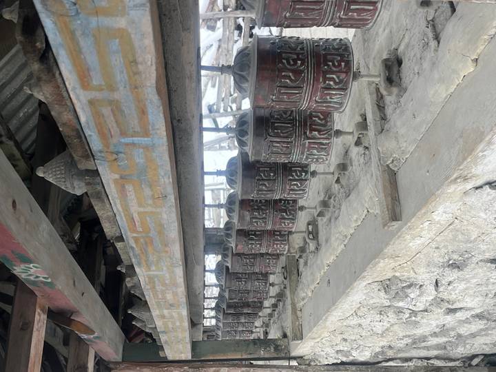 Row of traditional Tibetan prayer wheels mounted on a wooden frame along a mountain trail