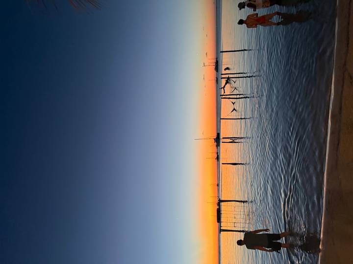 Calm sunset over the sea with hammocks suspended from poles and sailboats silhouetted on the horizon.