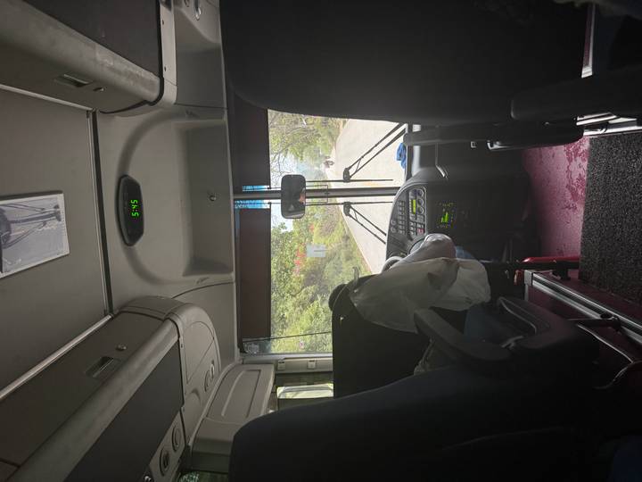 View from inside a coach looking through the windshield onto a rural road during transit.