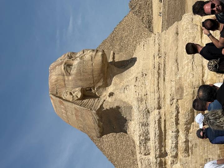 Side profile of the Great Sphinx of Giza with pyramid stones in the background under blue sky.