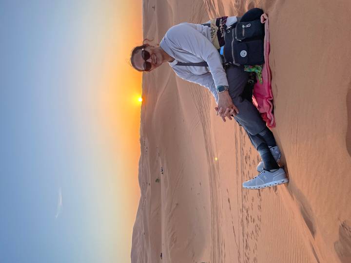 Woman sits relaxed on a blanket watching the sun set over endless rolling sand dunes.