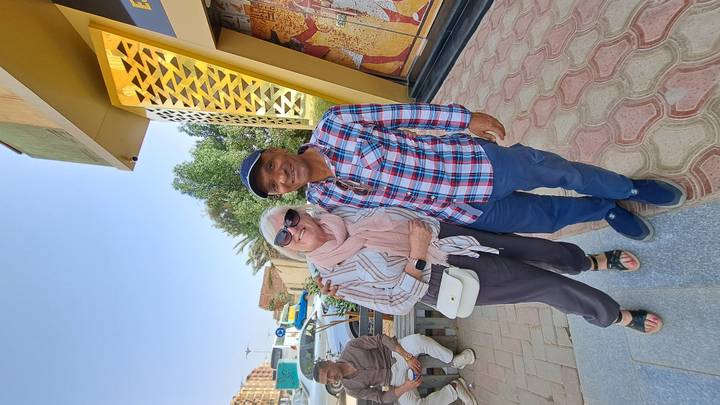 Older female traveler poses with an Egyptian local guide outside a modern museum entrance.