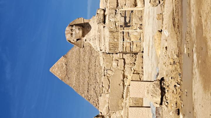The Sphinx sits before a pyramid with clear delineation under bright sunlight in Giza.