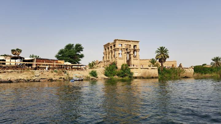 Ancient Philae Temple complex rises from the Nile’s edge surrounded by palm trees and calm water.