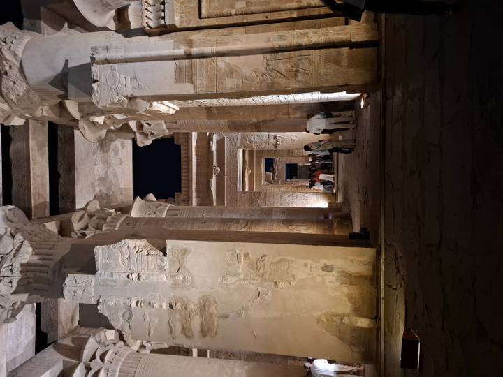 Dramatic nighttime view down a colonnaded hall of an ancient Egyptian temple lit by spotlights.