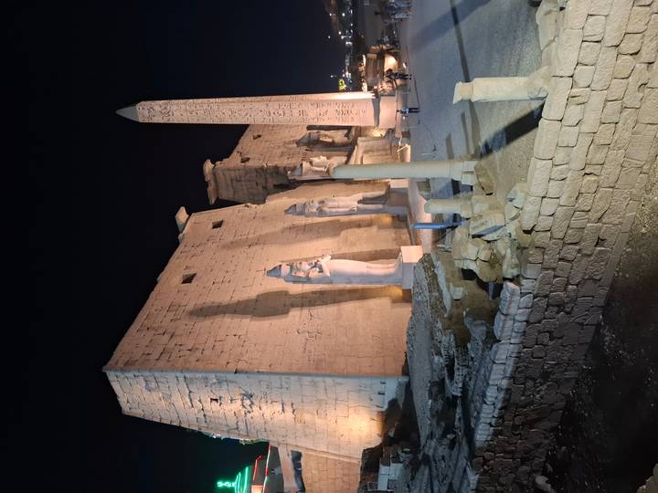 Luxor Temple illuminated at night with colossal statues and towering obelisk casting long shadows.