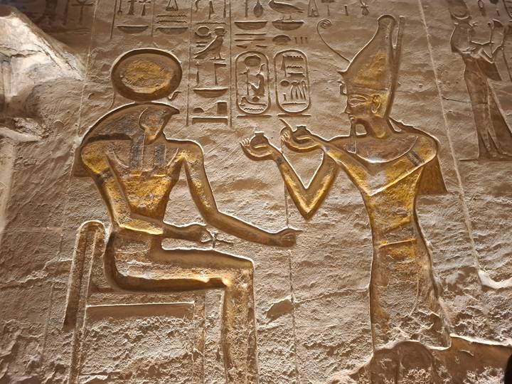 Close-up of golden relief depicting two ancient Egyptian deities exchanging offerings.