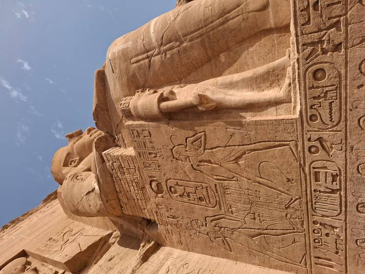 Detailed carving of pharaoh and hieroglyphs on the massive façade of Abu Simbel under blue sky.