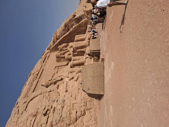 Wide shot of the Abu Simbel temple complex carved into sandstone cliffs with visitors exploring.
