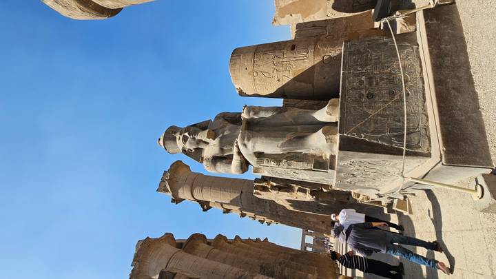 Massive seated pharaoh statue and papyrus-shaped columns inside Luxor Temple courtyard.