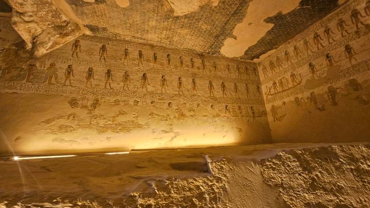 Dimly lit tomb chamber walls covered with detailed ancient Egyptian hieroglyphs and figures.