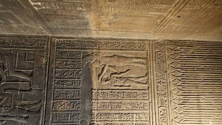 Carved stone reliefs with hieroglyphic columns inside a temple nook lit by warm light.