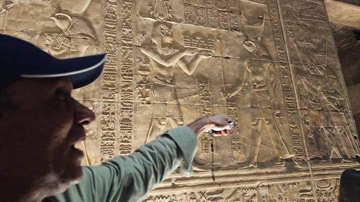 Close-up of a guide pointing out detailed hieroglyphs carved into a sandstone wall.