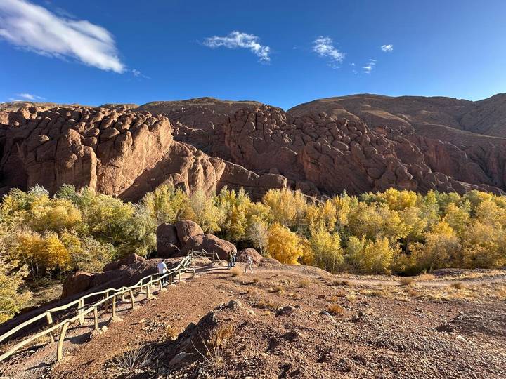 Rocky cliff formations above a valley of autumn-colored trees with a wooden viewing deck and visitors.