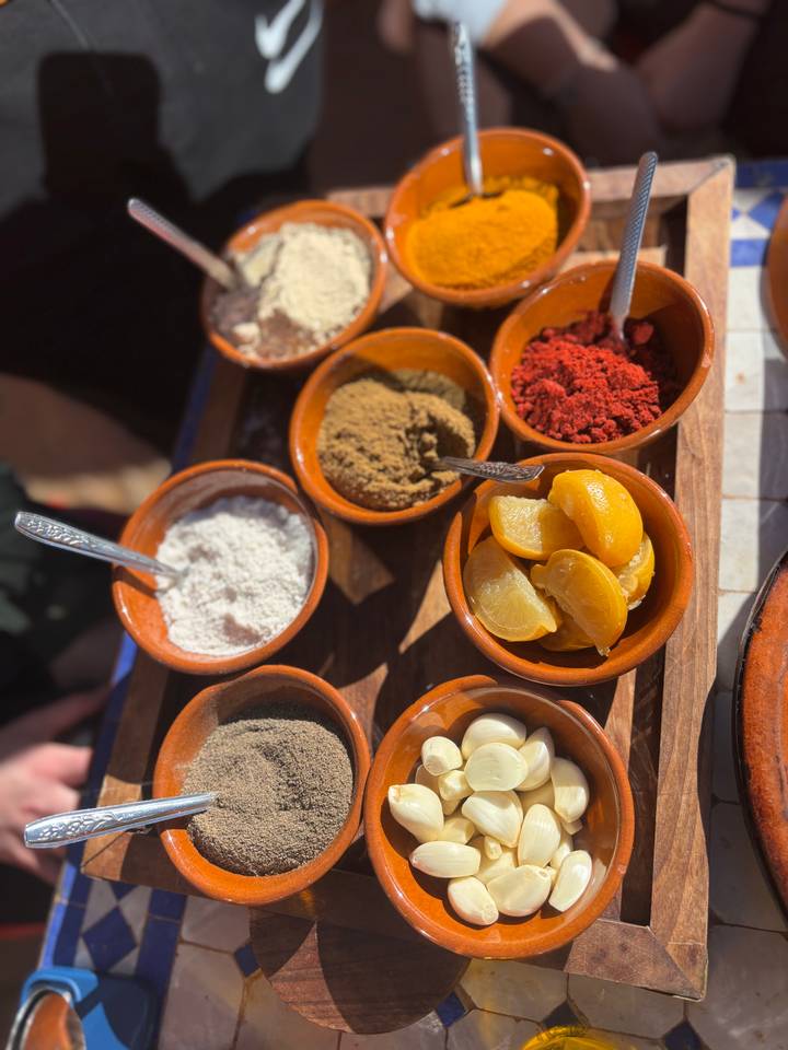 Close-up of assorted Moroccan spices and preserved lemons in small clay bowls.