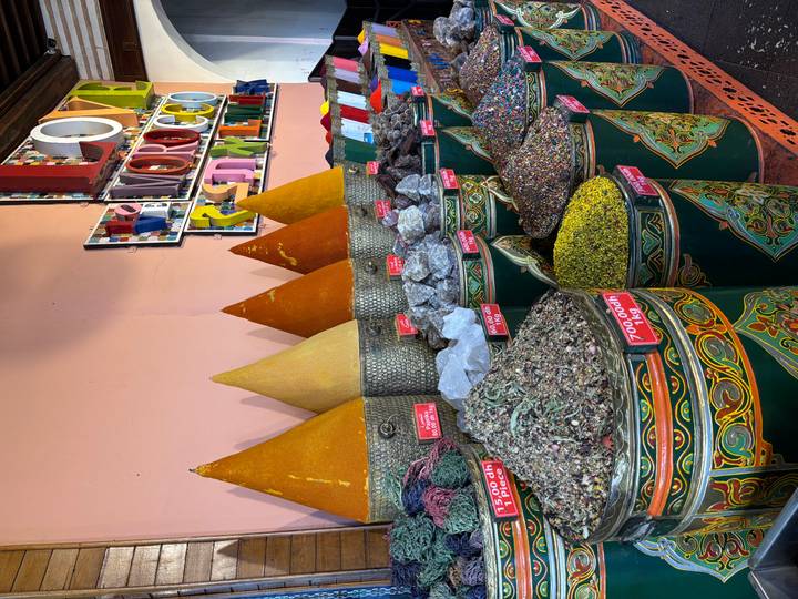 Colorful cones of spices, dried herbs and minerals displayed in ornate metal barrels inside a Moroccan shop.