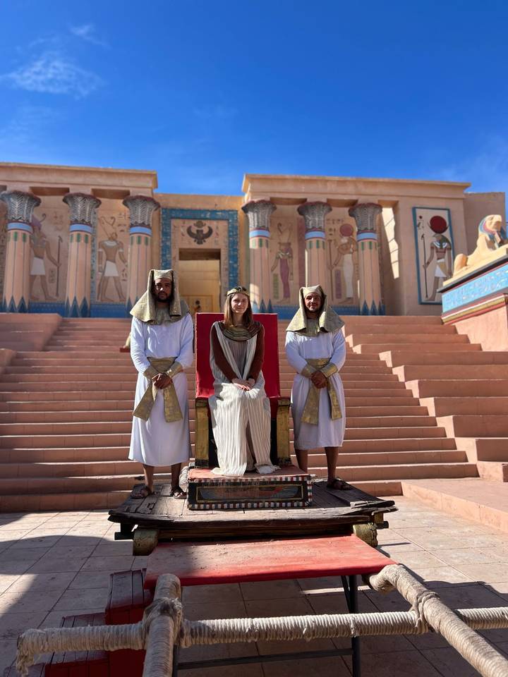 Tourist seated on a throne flanked by two men in ancient Egyptian costumes at a movie set.