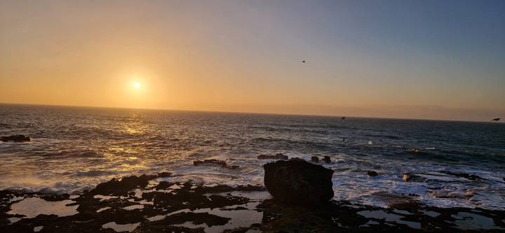 Sun setting over the Atlantic Ocean with waves crashing against rocky shoreline.