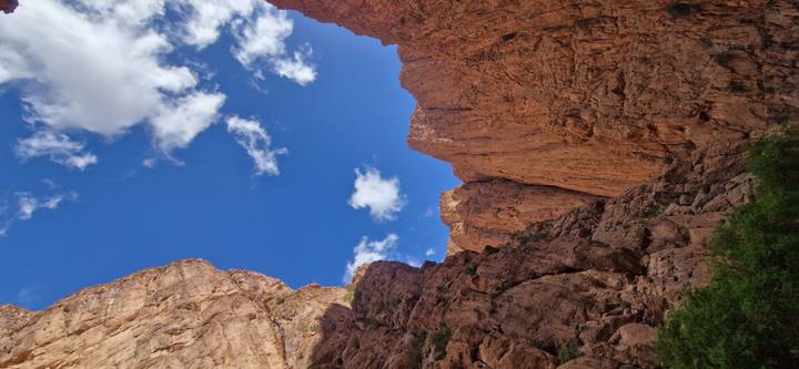 Steep red rock canyon walls and blue sky viewed from the gorge floor.