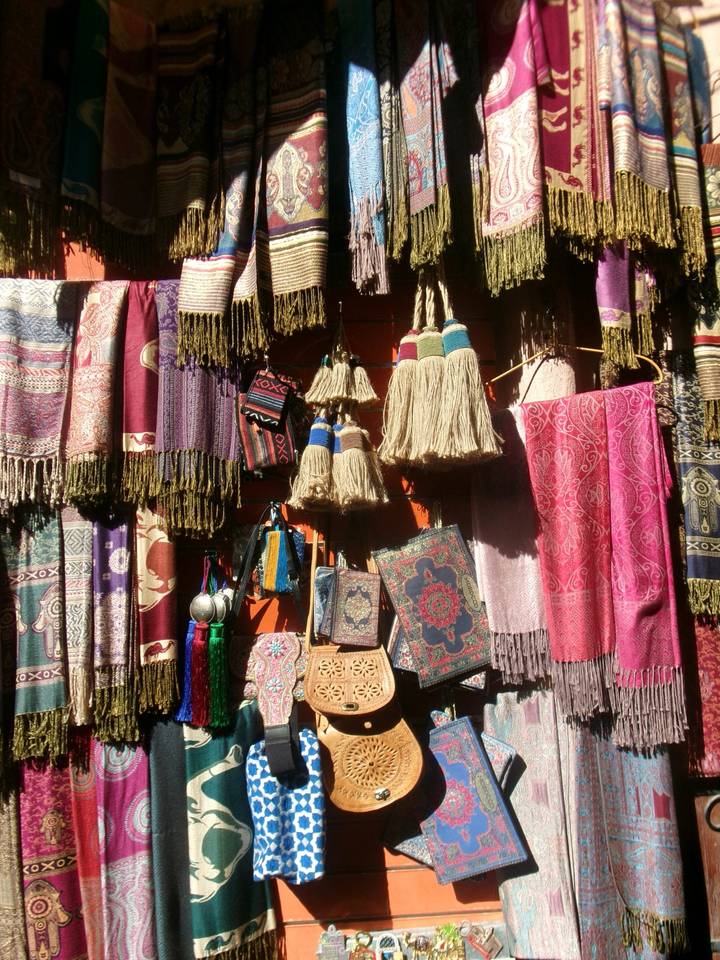 An array of colourful woven scarves, tassels and embroidered bags hanging at a Moroccan souk stall.