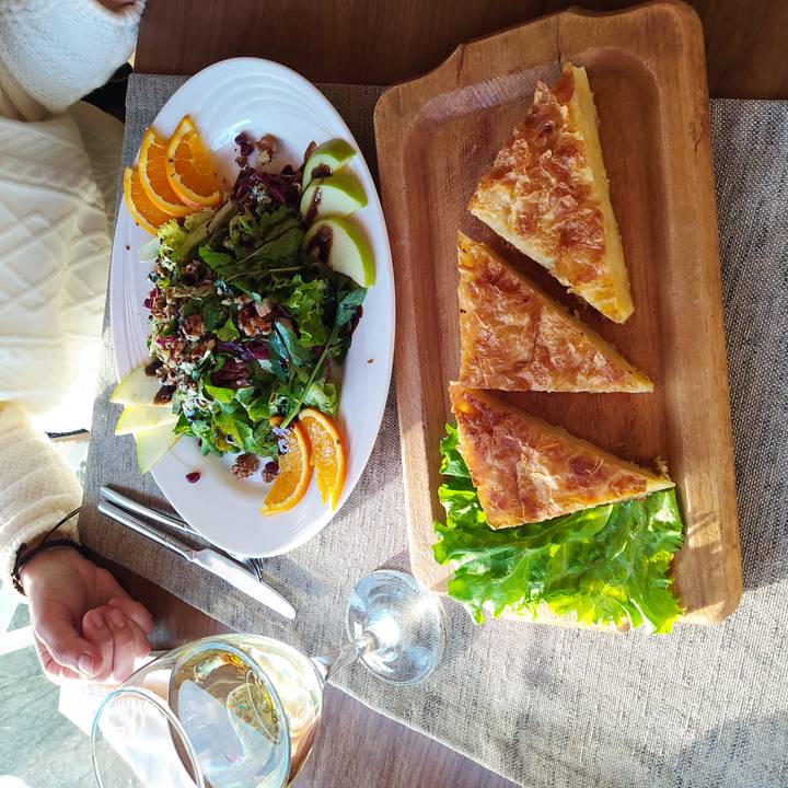 Fresh salad with oranges and walnuts plus slices of savoury pie served on wooden boards at a sunlit table.