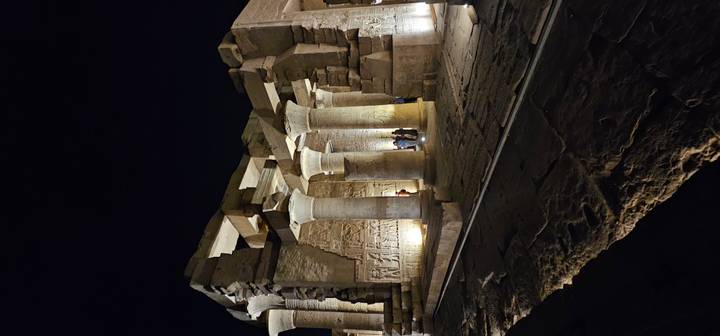 Illuminated columns and reliefs of an ancient temple standing against night sky