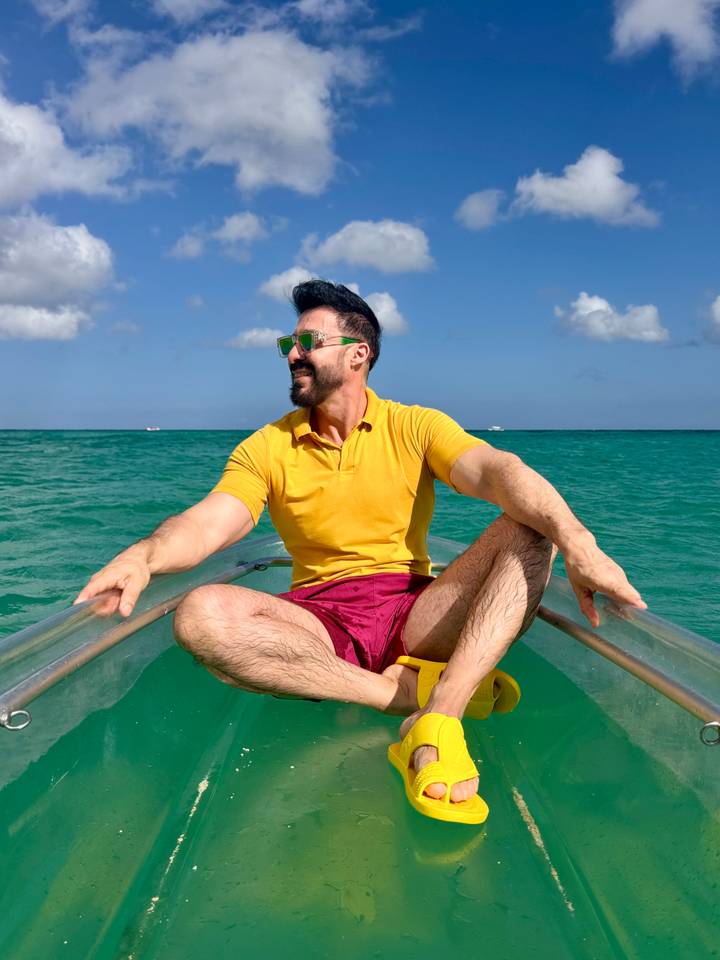 Man in clear kayak smiles over turquoise tropical waters under blue sky.