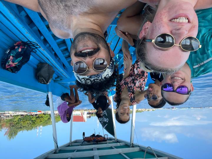 Cheerful group selfie on bright blue wooden boat cruising calm tropical waters.