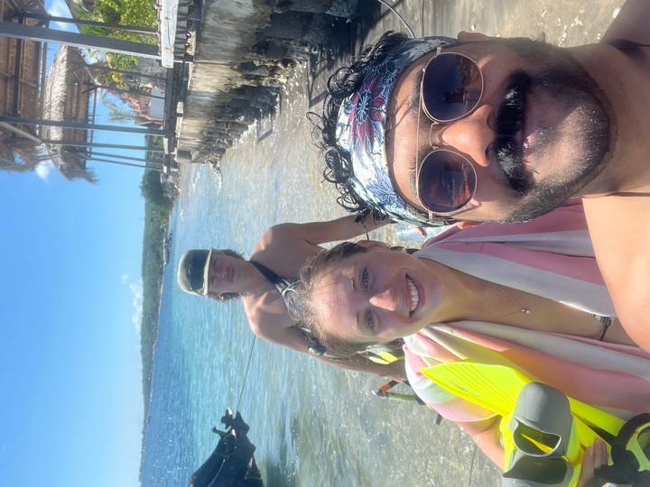 Friends take beach selfie with snorkel gear on sunny shoreline.