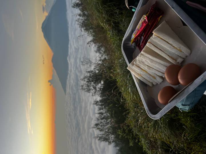 Breakfast tray with sandwiches and eggs overlooks sea of clouds and volcanic peaks at dawn.
