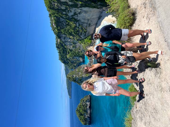 Friends celebrate at stunning seaside cliff viewpoint with vibrant turquoise waters below on Nusa Penida.