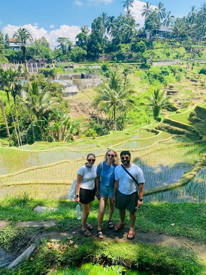 Three travelers smile together in front of tiered rice terraces near Ubud.