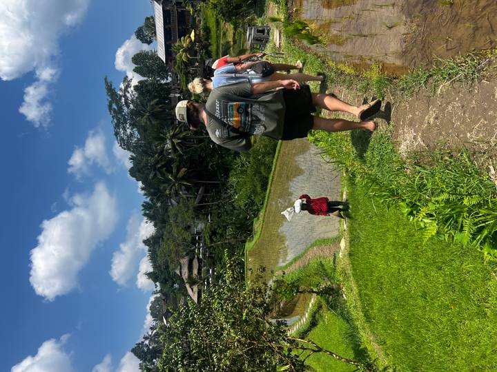 Group walks narrow path along rice paddies while local farmer works below.