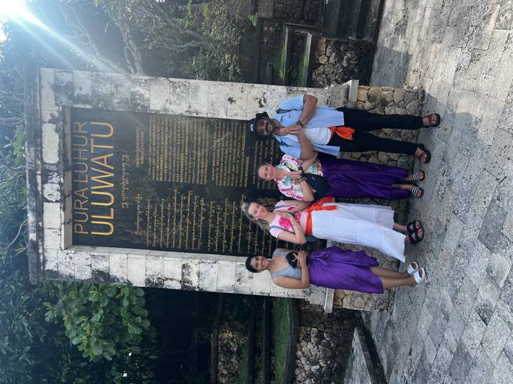 Group stands in front of large Pura Luhur Uluwatu information sign wearing temple attire.