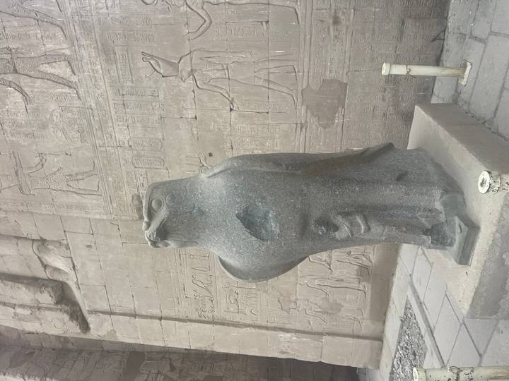 Granite falcon statue of Horus stands before hieroglyph-covered temple wall in Edfu.