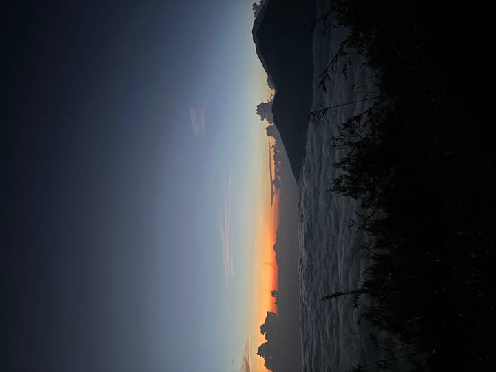 Pre-dawn view of sea of clouds below silhouetted volcano ridgeline with colorful horizon glow.