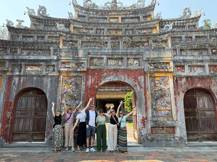 Travel group raises arms in celebration before an ornately carved gate at Hue’s Imperial City.