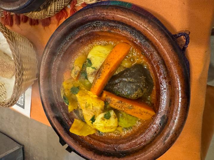 Steaming Moroccan tagine with vegetables and meat served in traditional clay pot