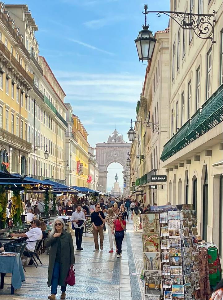 Bustling Rua Augusta in Lisbon lined with colourful façades, café umbrellas and the iconic Arco da Rua Augusta at the end.