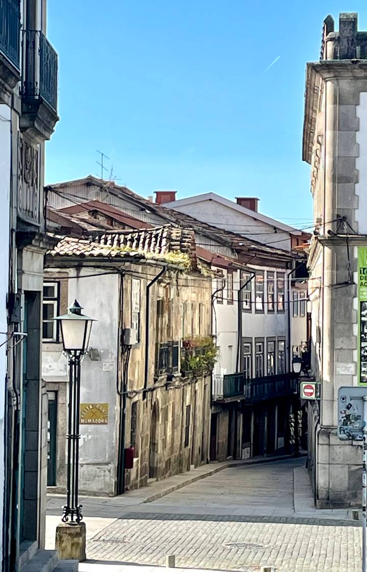 Aged rooftops and weathered façades in a narrow Portuguese alleyway with vintage streetlamp.
