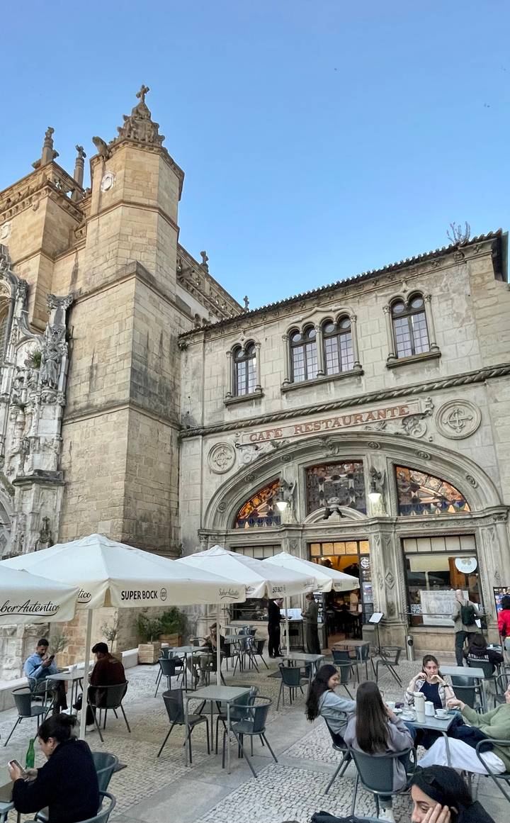 Stone church façade with arched windows and a vintage sign reading 'Café Restaurante' in Coimbra.