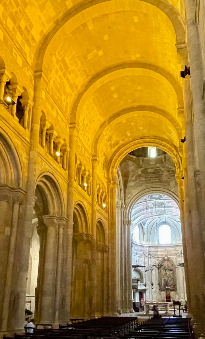 Warmly lit Romanesque cathedral interior featuring high stone arches and a distant painted apse ceiling.
