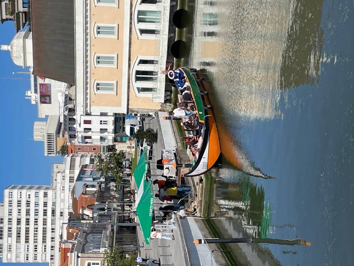Traditional moliceiro boat full of passengers gliding along Aveiro’s canal under clear blue skies.