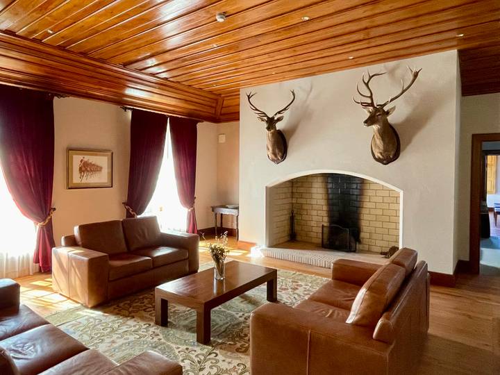 Rustic lounge with leather sofas, a brick fireplace and mounted deer heads in a country manor.
